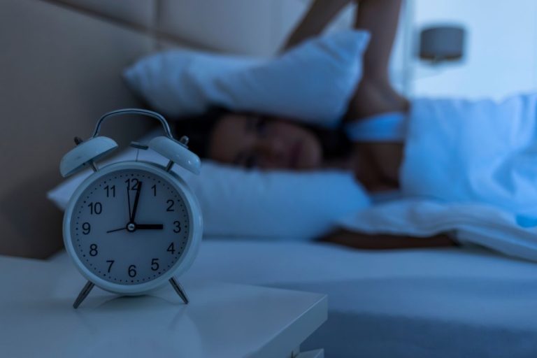 Person struggling to sleep and alarm clock representing insomnia and sleep apnea.