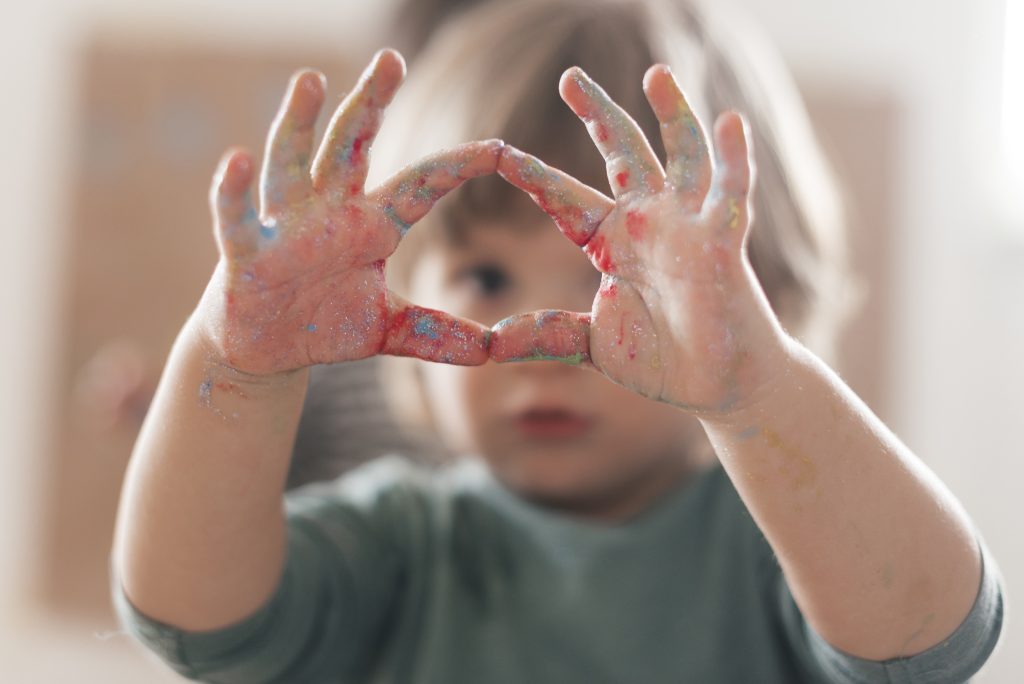 Autistic child with paint-covered hands forming a heart shape, addressing frustration and aggression.