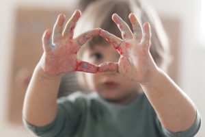 Frustrated autistic child with paint-covered hands forming a frame, seeking help and support.